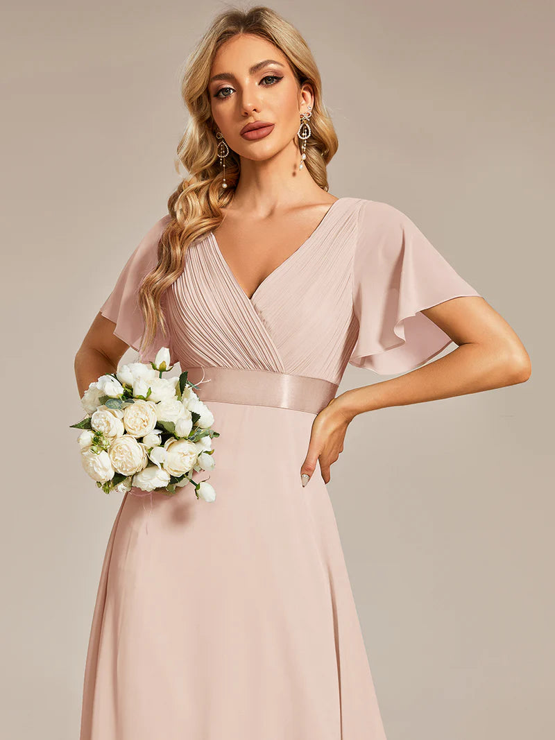 Woman in a dusty rose dress holding a bouquet of flowers against a beige background
