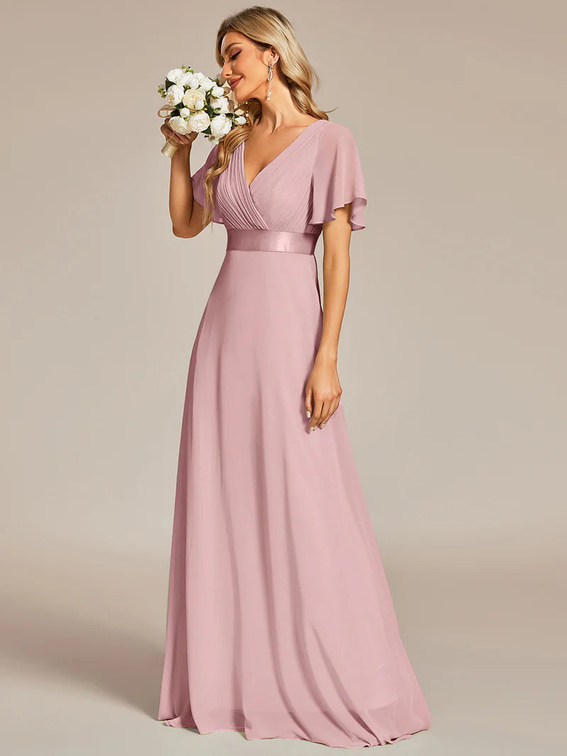 Woman wearing a dusty rose gown holding flowers against a beige background