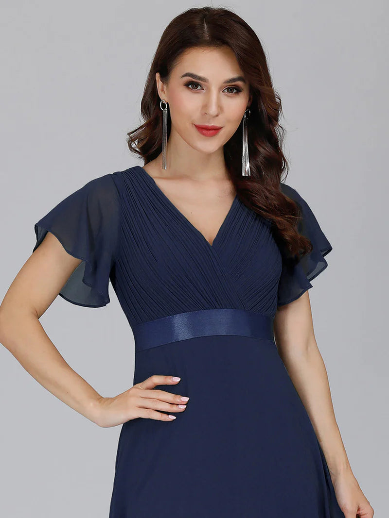 Woman wearing a navy blue dress with sheer sleeves against a gray background