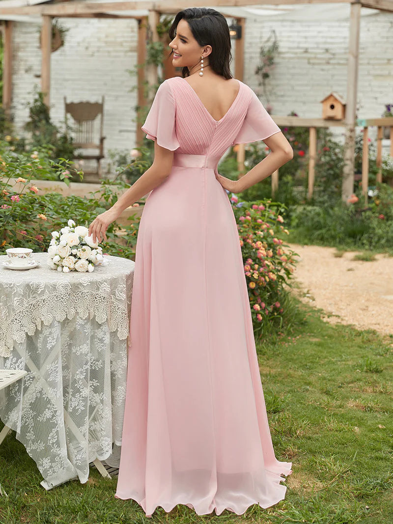 Woman in a dusty rose dress standing outdoors near a table with flowers.