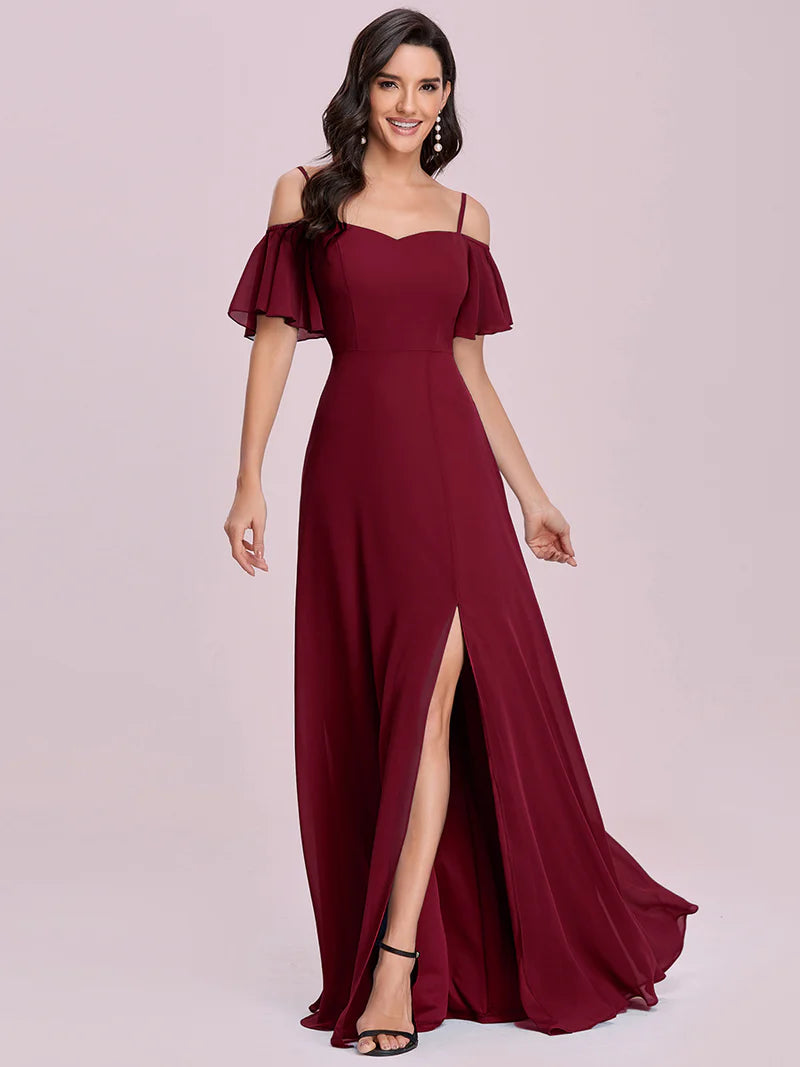 Woman wearing a burgundy off-shoulder gown with a slit on a light pink background