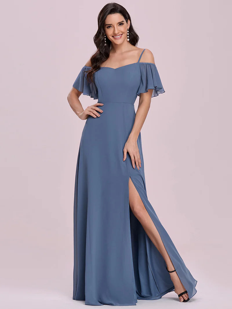 Woman wearing a dusty blue off-shoulder gown with a slit on a light pink background