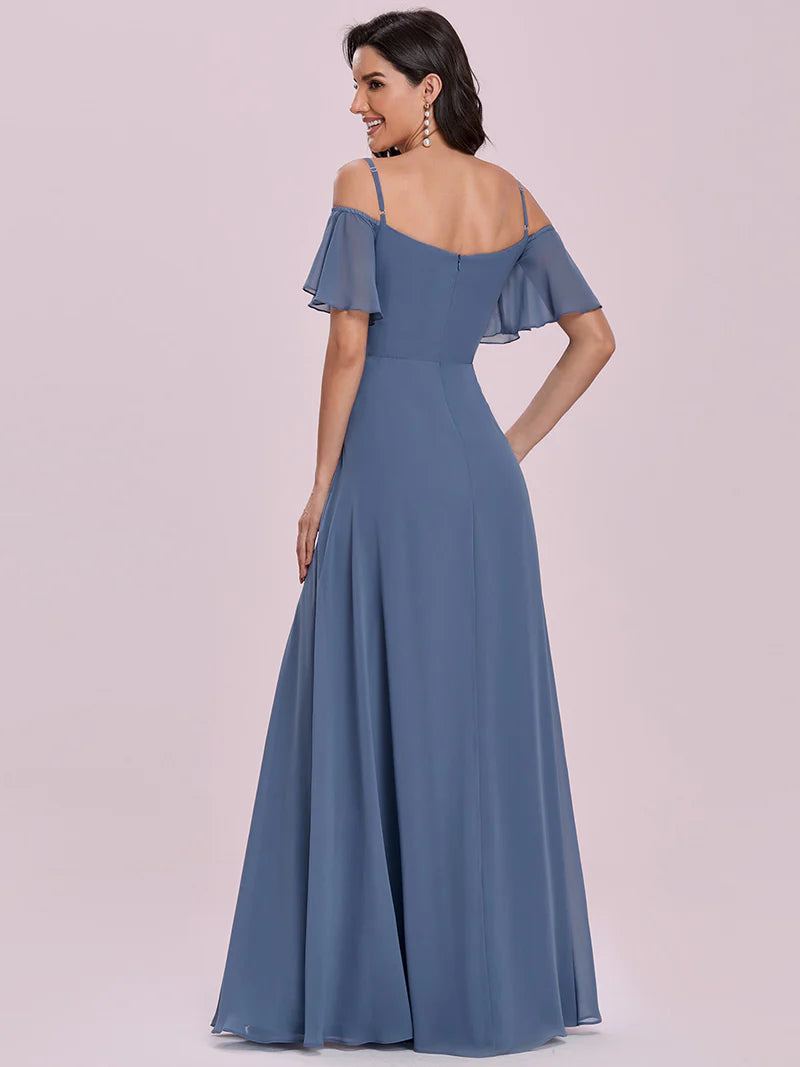 Woman wearing a dusty blue evening gown with ruffled sleeves on a light pink background