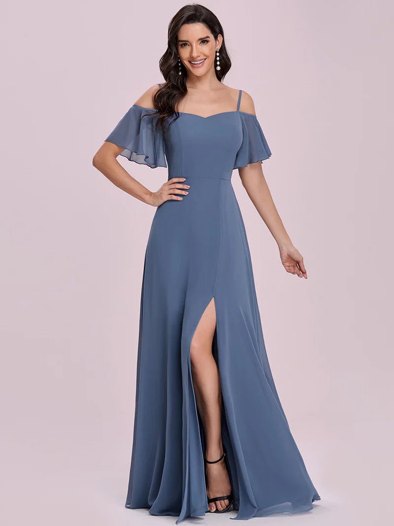 Woman wearing a dusty blue off-shoulder gown with a slit on a light pink background