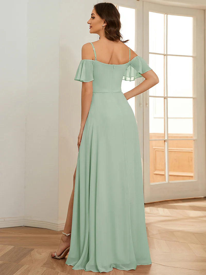 Woman wearing a mint green off-shoulder dress with a slit in a room with wooden flooring and white walls.