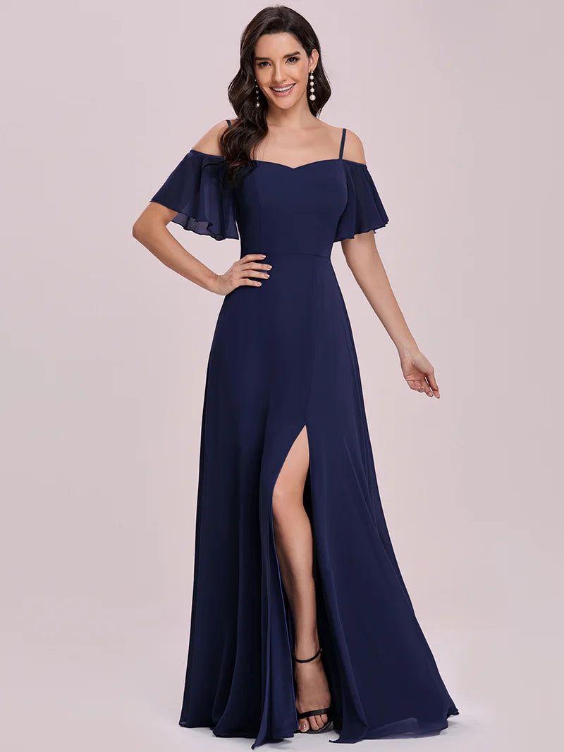 Woman wearing a navy blue off-shoulder gown with a slit on a light pink background
