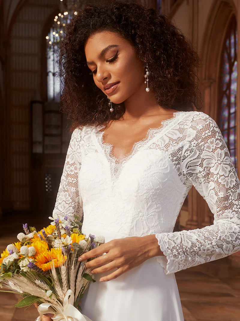 Woman in a white lace wedding dress holding a bouquet indoors.