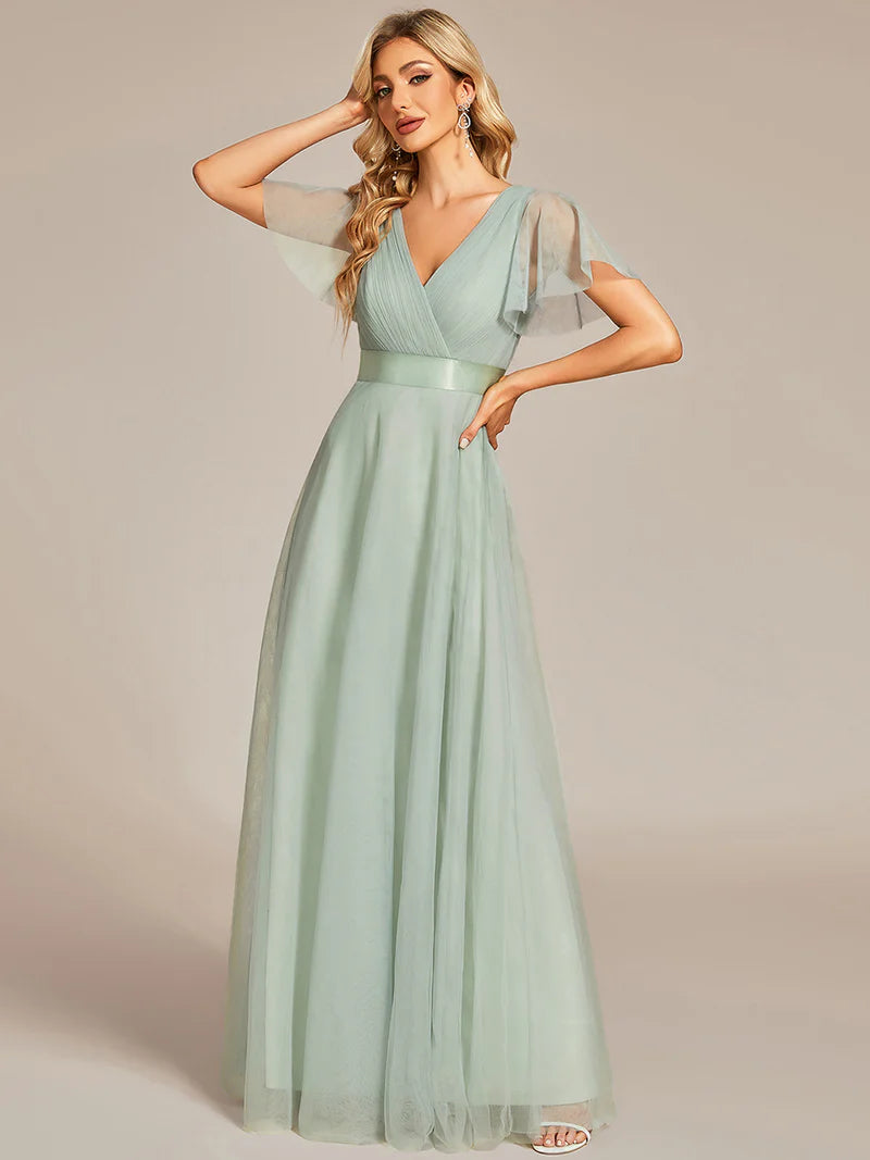Woman wearing a mint green evening gown with sheer sleeves against a beige background