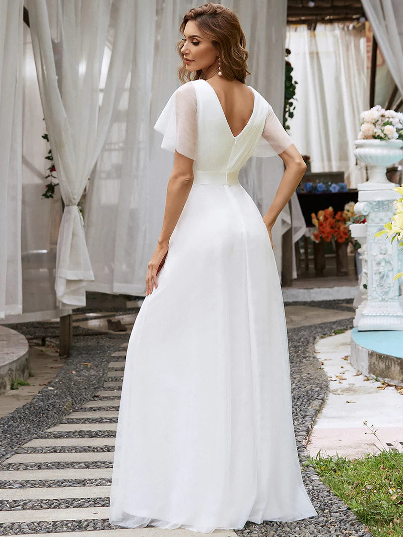 Woman in a white wedding dress standing in an outdoor setting with curtains and flowers.