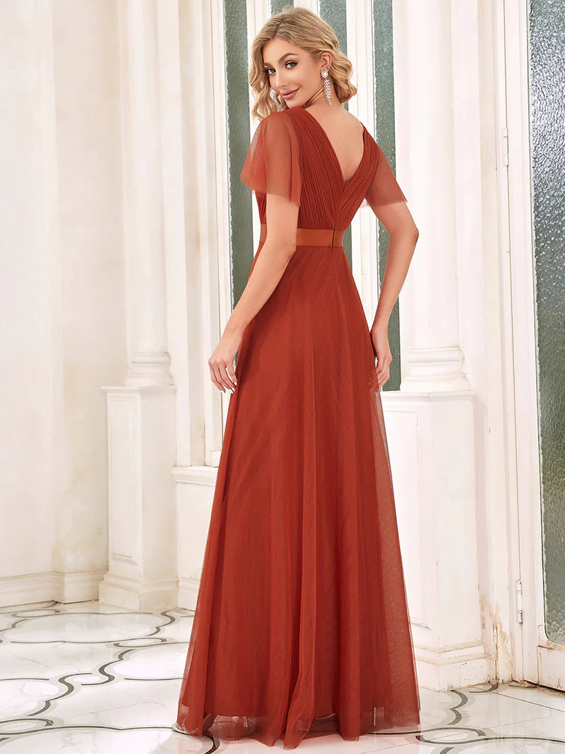 Woman wearing a burnt orange evening gown with a belt in an elegant interior setting.