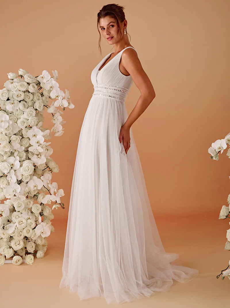 Woman in a ivory wedding dress standing against a peach background with floral decorations.