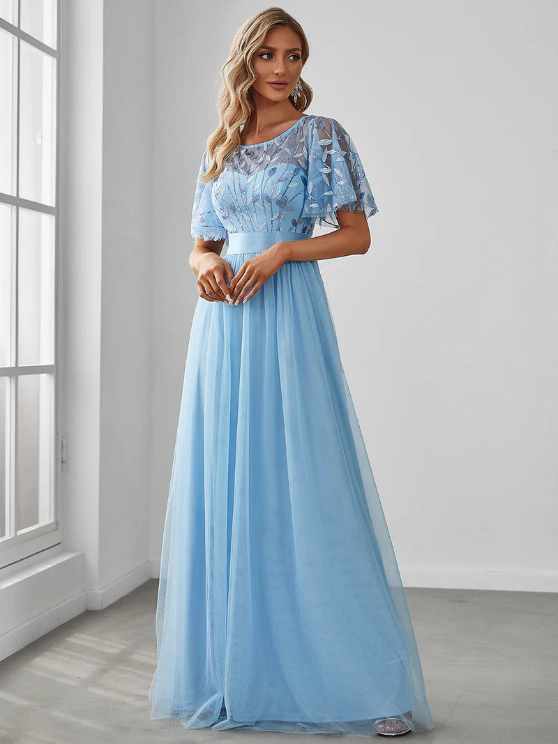 Woman wearing a light blue dress with lace detailing in a room with a window.