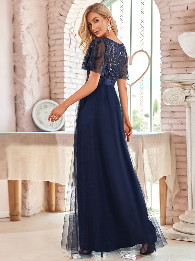 Woman wearing a long navy blue dress with lace details in an elegant indoor setting.
