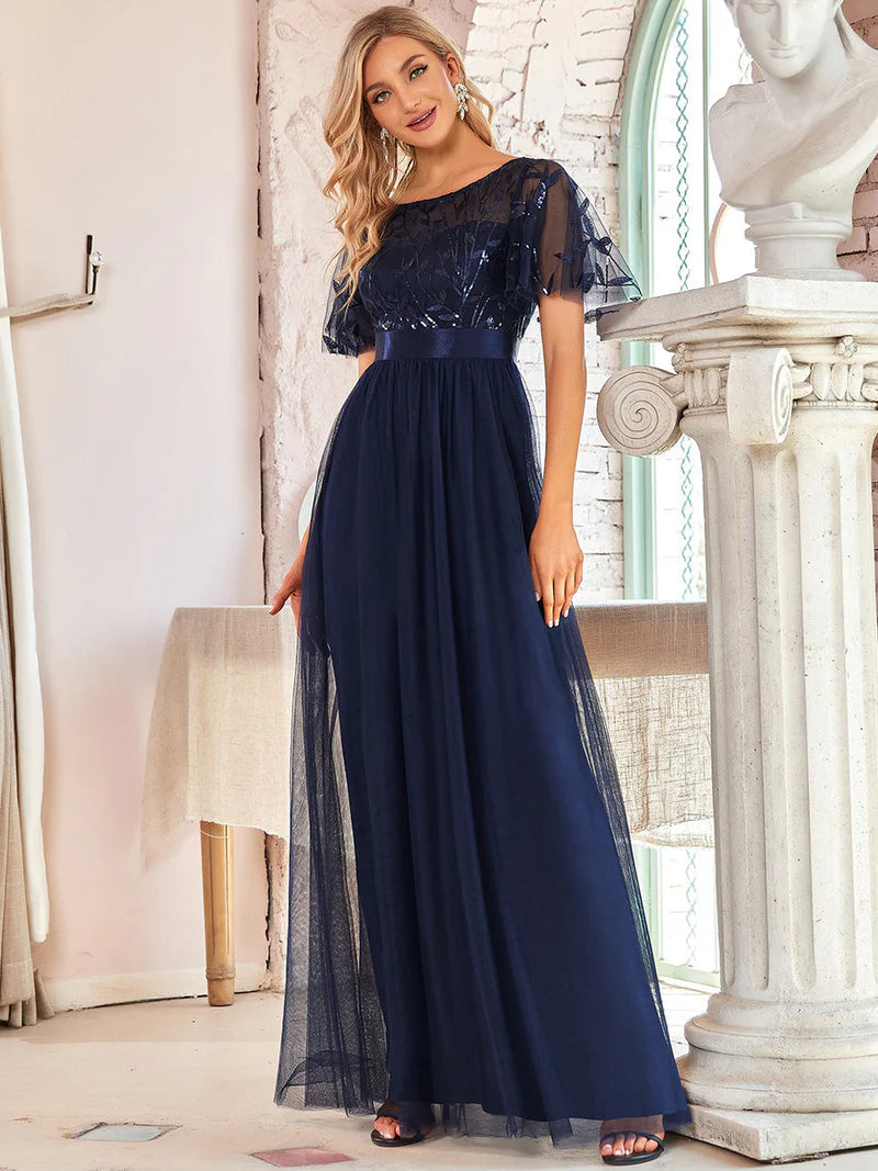 Woman wearing a navy blue evening gown with lace details in an elegant indoor setting.