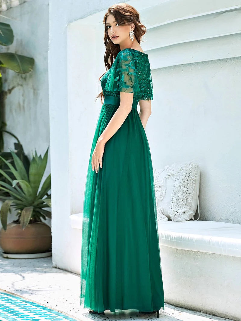 Woman wearing a green evening gown with lace details in an outdoor setting.