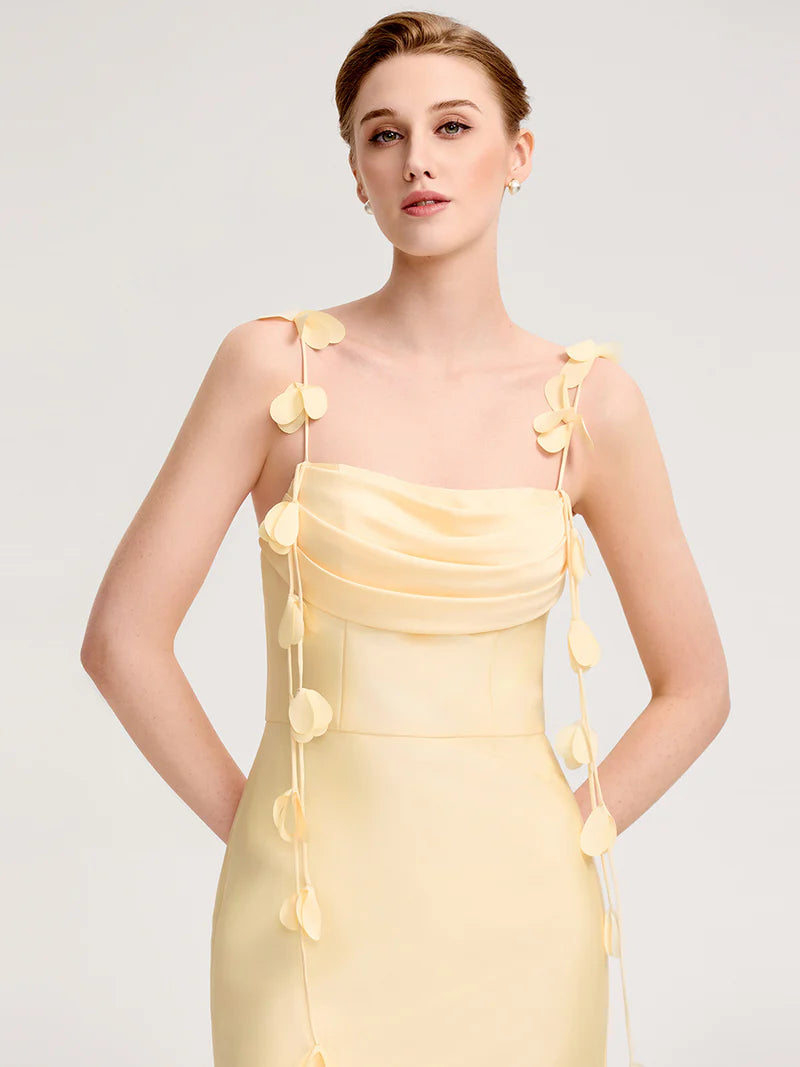Woman wearing a yellow dress with floral details on a plain background