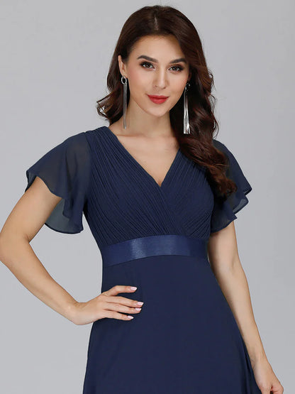 Woman wearing a navy blue dress with sheer sleeves against a gray background
