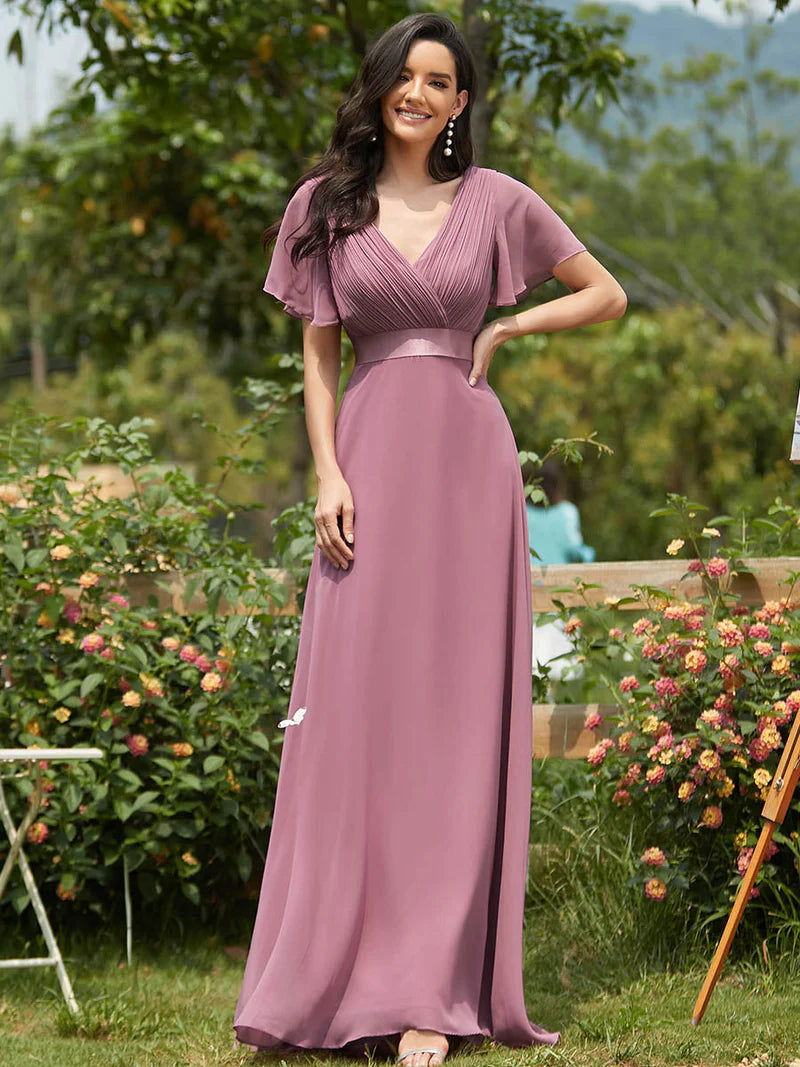 Woman in a long orchid dress standing outdoors with greenery and flowers in the background