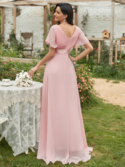 Woman in a dusty rose dress standing outdoors near a table with flowers.