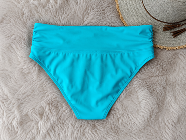 Turquoise bikini bottom on a fluffy gray surface with a straw hat in the background.