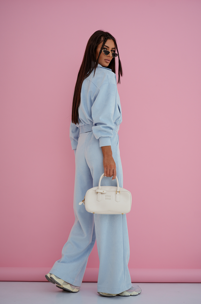 Woman in a light blue outfit holding a white handbag against a pink background