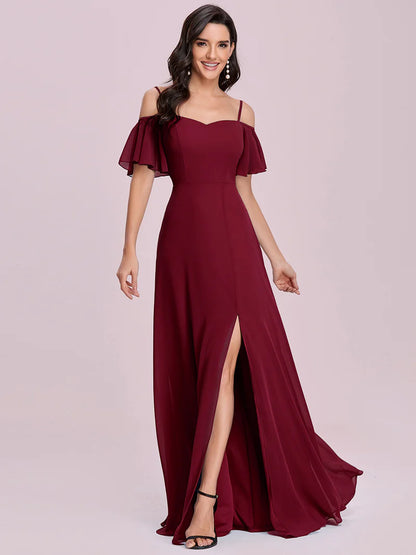 Woman wearing a burgundy off-shoulder gown with a slit on a light pink background