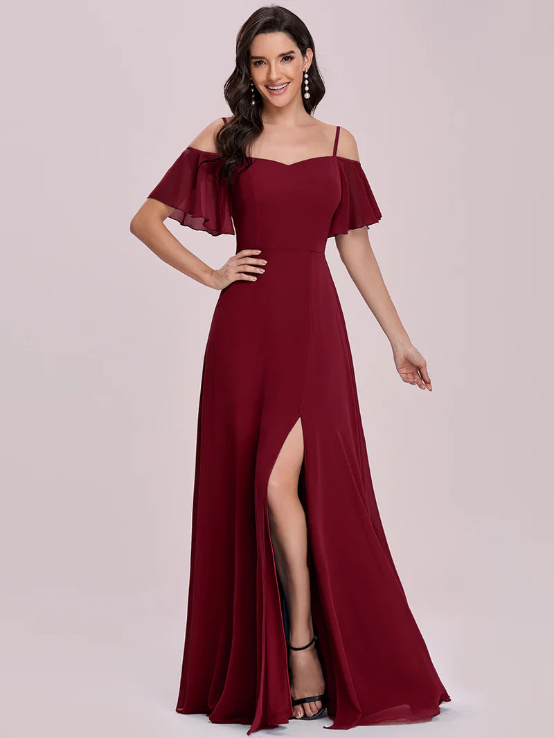 Woman wearing a burgundy off-shoulder gown with a slit on a light pink background