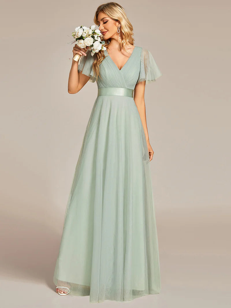 Woman wearing a mint  green dress holding flowers against a plain background