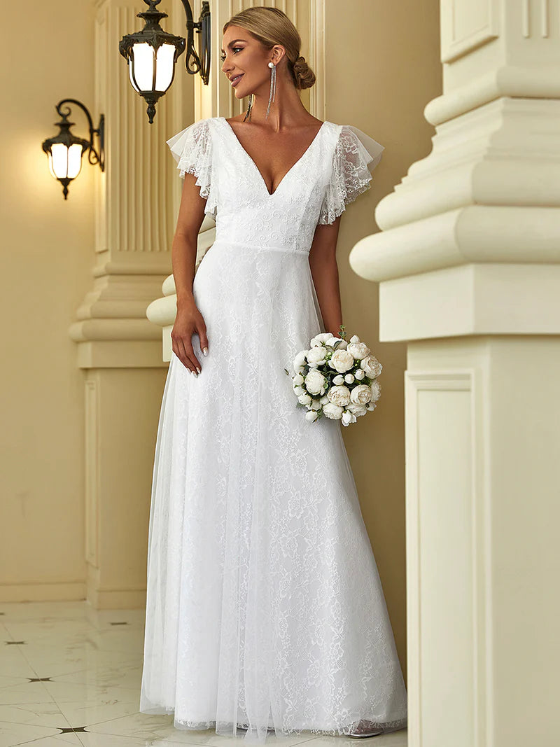 Woman in a white lace wedding dress holding flowers in an elegant indoor setting.