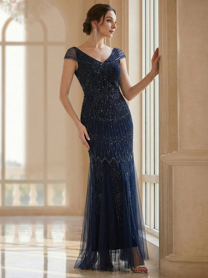 Woman in a navy blue evening gown standing in a room with large windows.