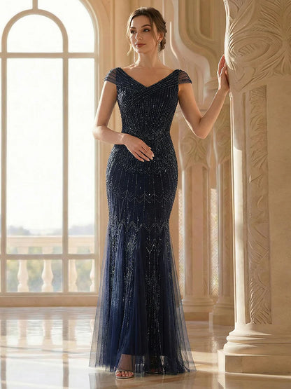 Woman in a navy blue evening gown standing in an elegant interior setting.