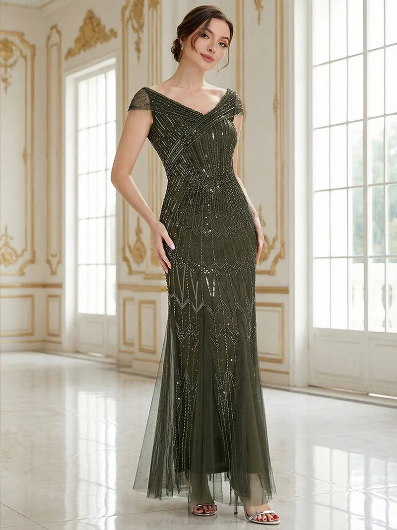 Woman in a long, olive green evening gown with beaded details in an elegant room.