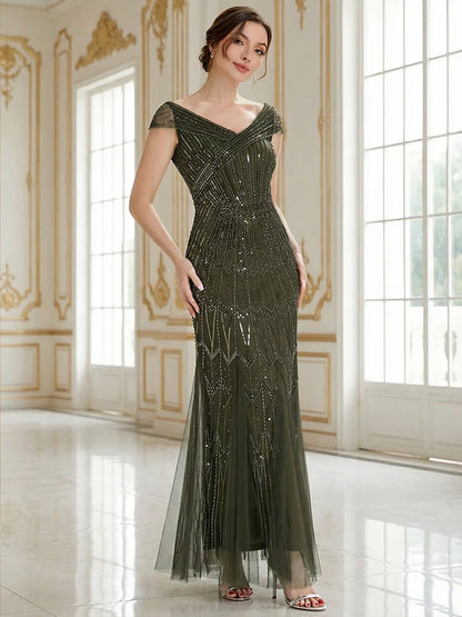 Woman in a long, olive green evening gown with beaded details in an elegant room.