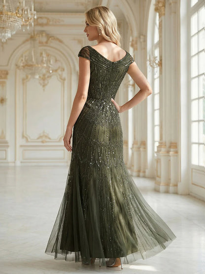 Woman in an elegant olive green evening gown with beaded details in a luxurious room.