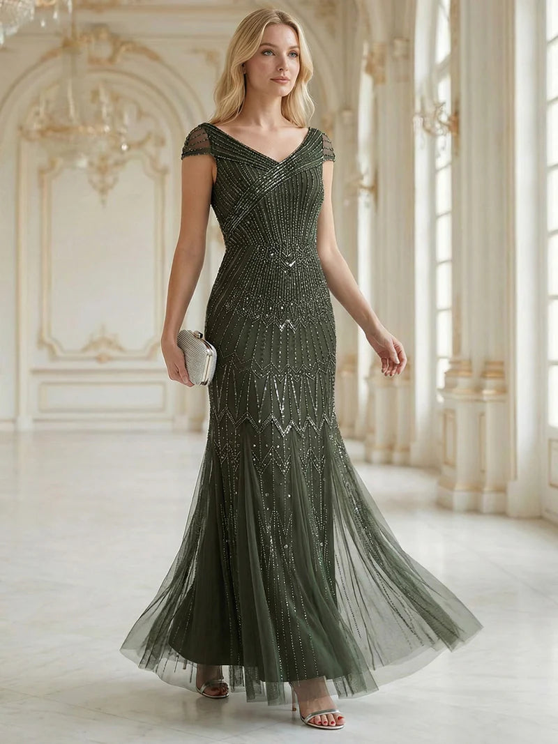 Woman in a olive green beaded evening gown standing in an elegant room.