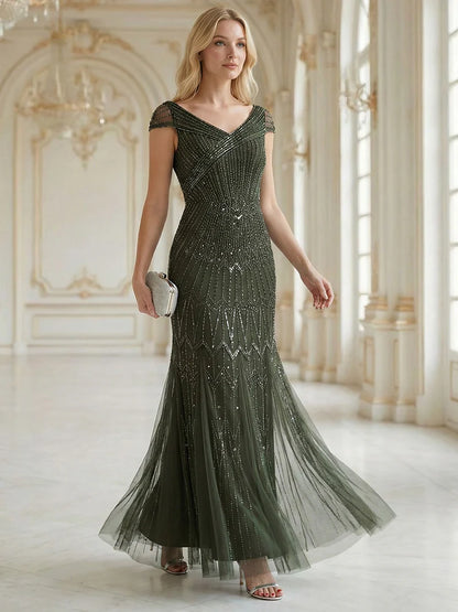 Woman in a olive green beaded evening gown standing in an elegant room.