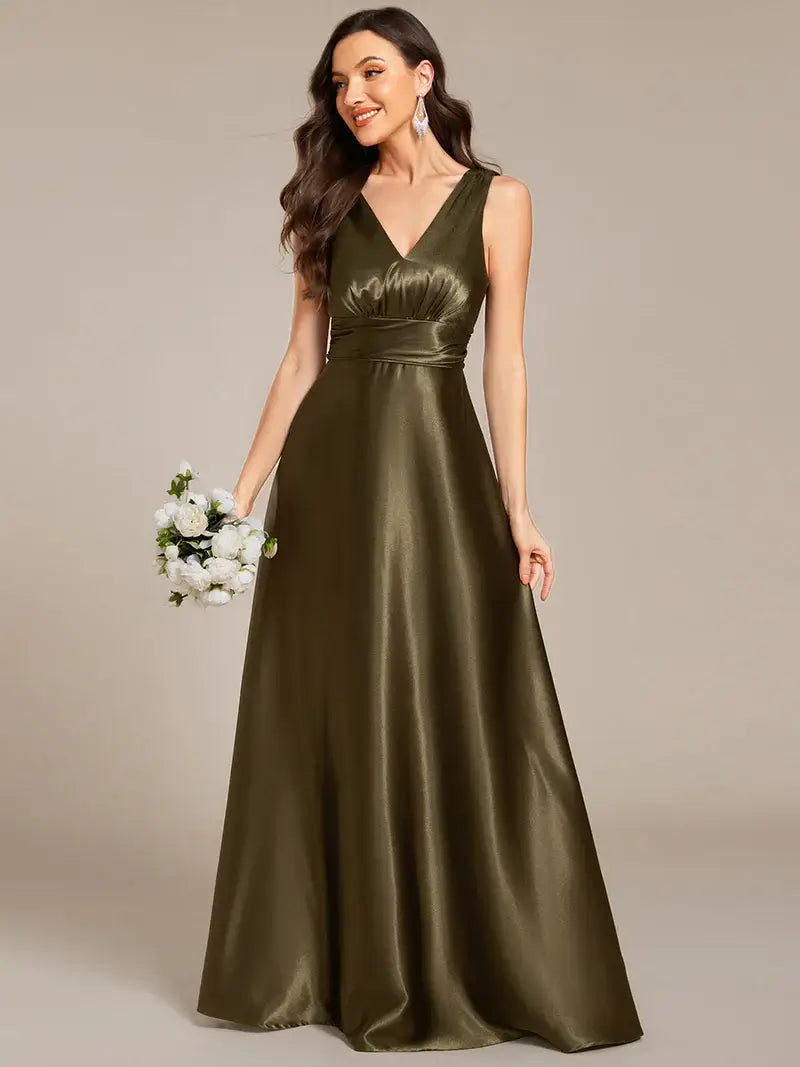 Woman wearing an olive green satin gown holding a bouquet against a beige background
