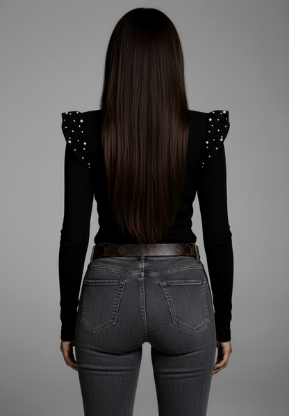 Person wearing a black top with shoulder embellishments and dark jeans on a gray background
