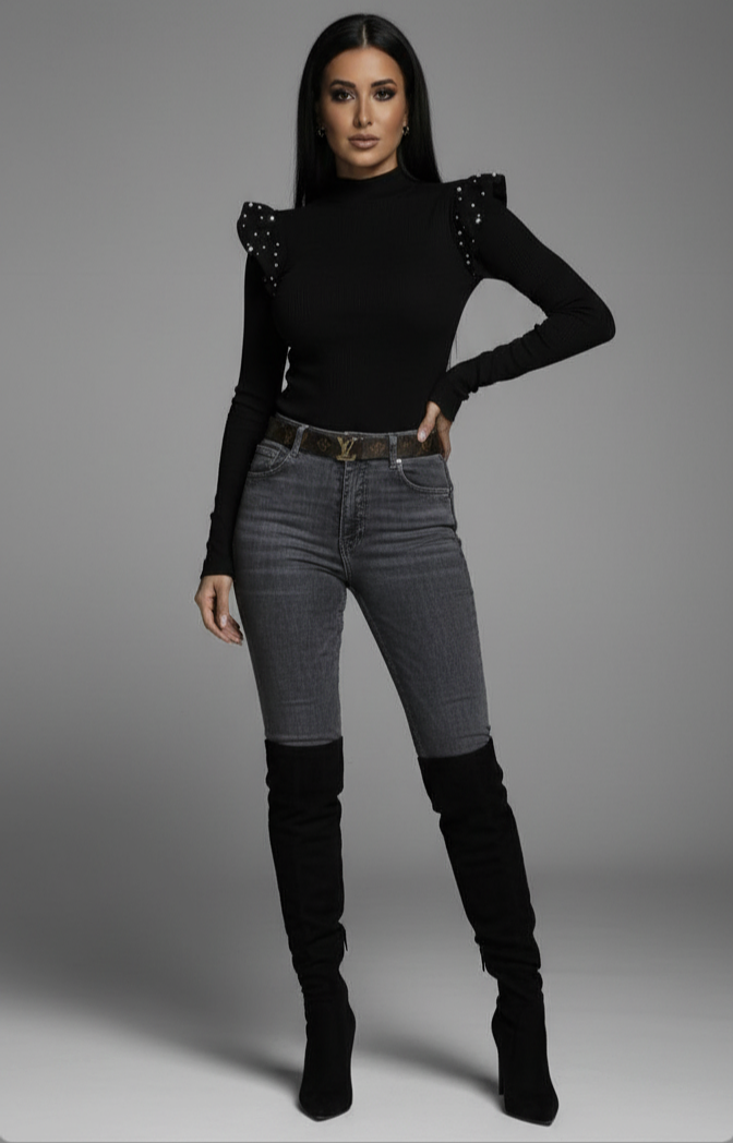 Woman wearing a black top with embellishments and gray jeans on a gray background