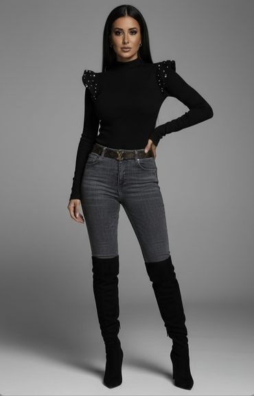 Woman wearing a black top with embellishments and gray jeans on a gray background