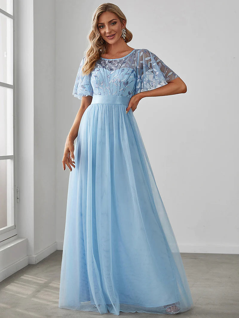 Woman wearing a light blue evening gown with lace top in a room with a window.