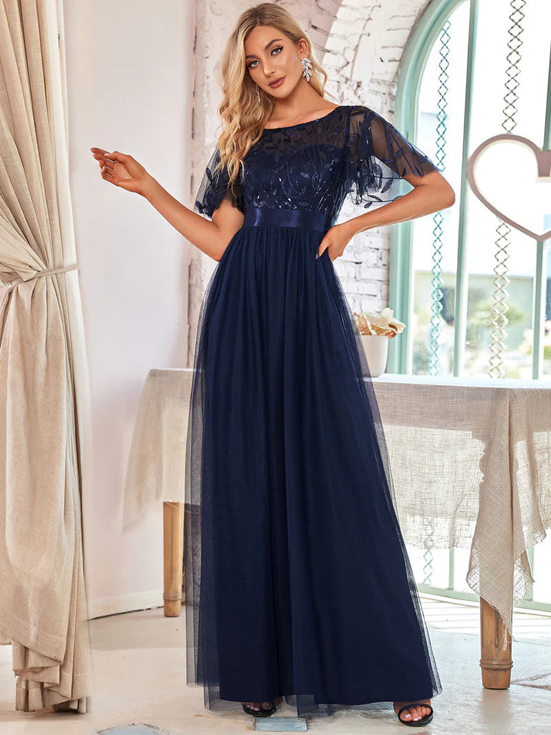 Woman wearing a navy blue evening gown with lace details in a bright room.