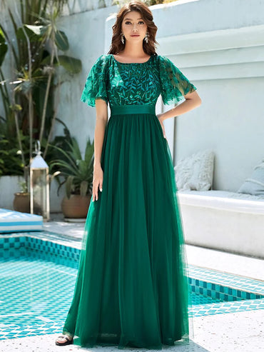 Woman in a green evening gown standing by a poolside.