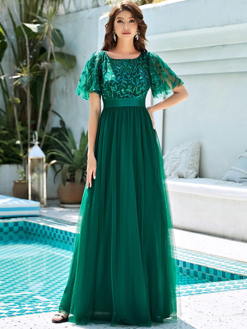 Woman in a green evening gown standing by a poolside.