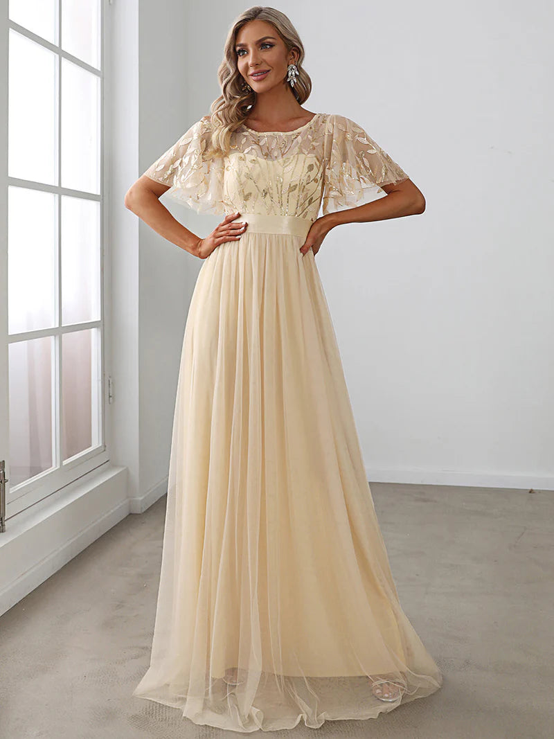 Woman wearing a gold evening gown in a room with a window.