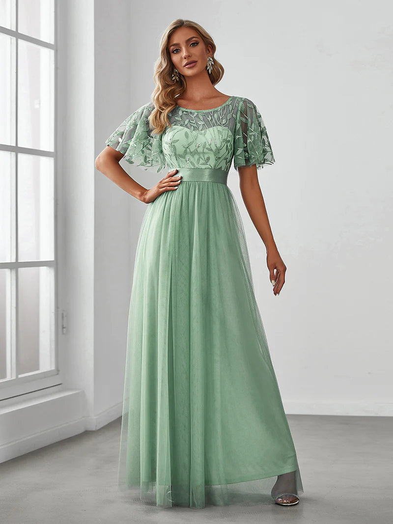 Woman wearing a mint green lace dress standing in a room with a window.