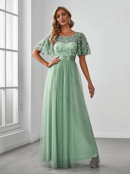 Woman wearing a mint green lace dress standing in a room with a window.