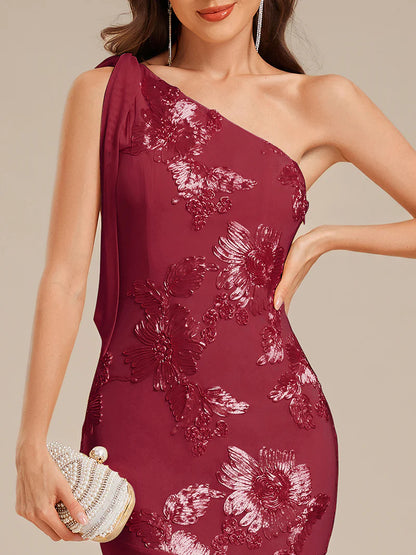 Woman wearing a burgundy one-shoulder dress with floral patterns on a beige background