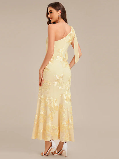 Woman wearing a yellow one-shoulder dress with floral patterns on a beige background