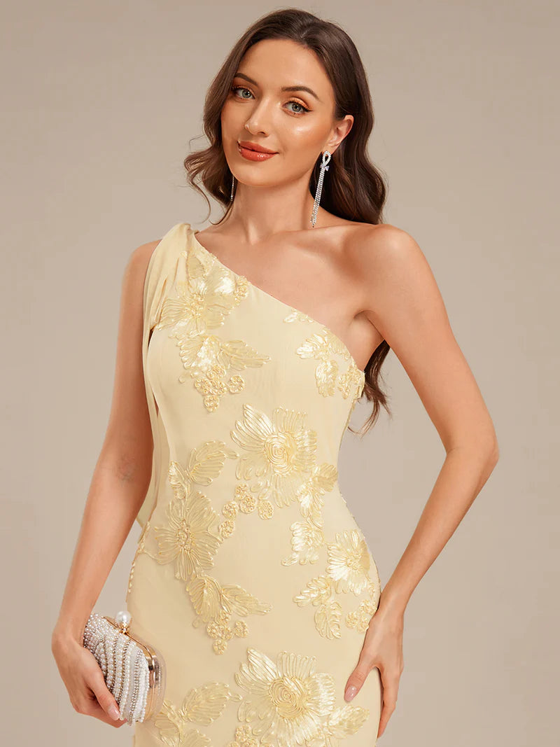 Woman wearing a beige one-shoulder dress with floral embroidery on a beige background